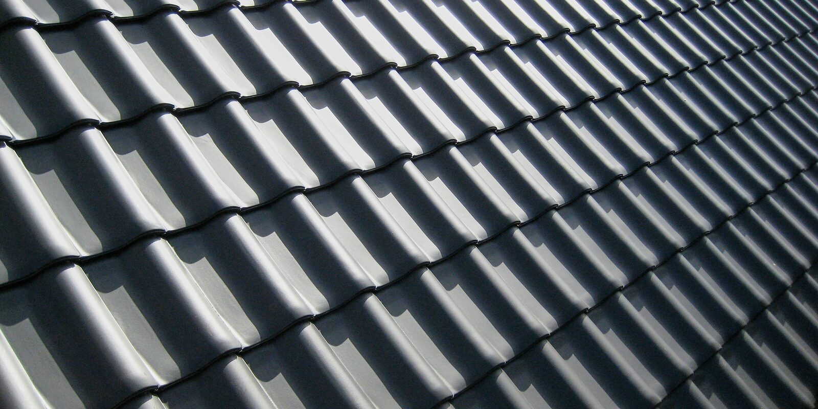 Close-up of a roof slope covered in dark grey interlocking concrete tiles, the courses running in even diagonal lines across the frame.