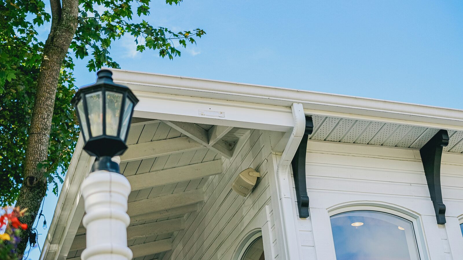 The overhanging eaves of a white weatherboarded building seen from below, showing the soffit, fascia and the shaped brackets carrying them, against a clear sky.